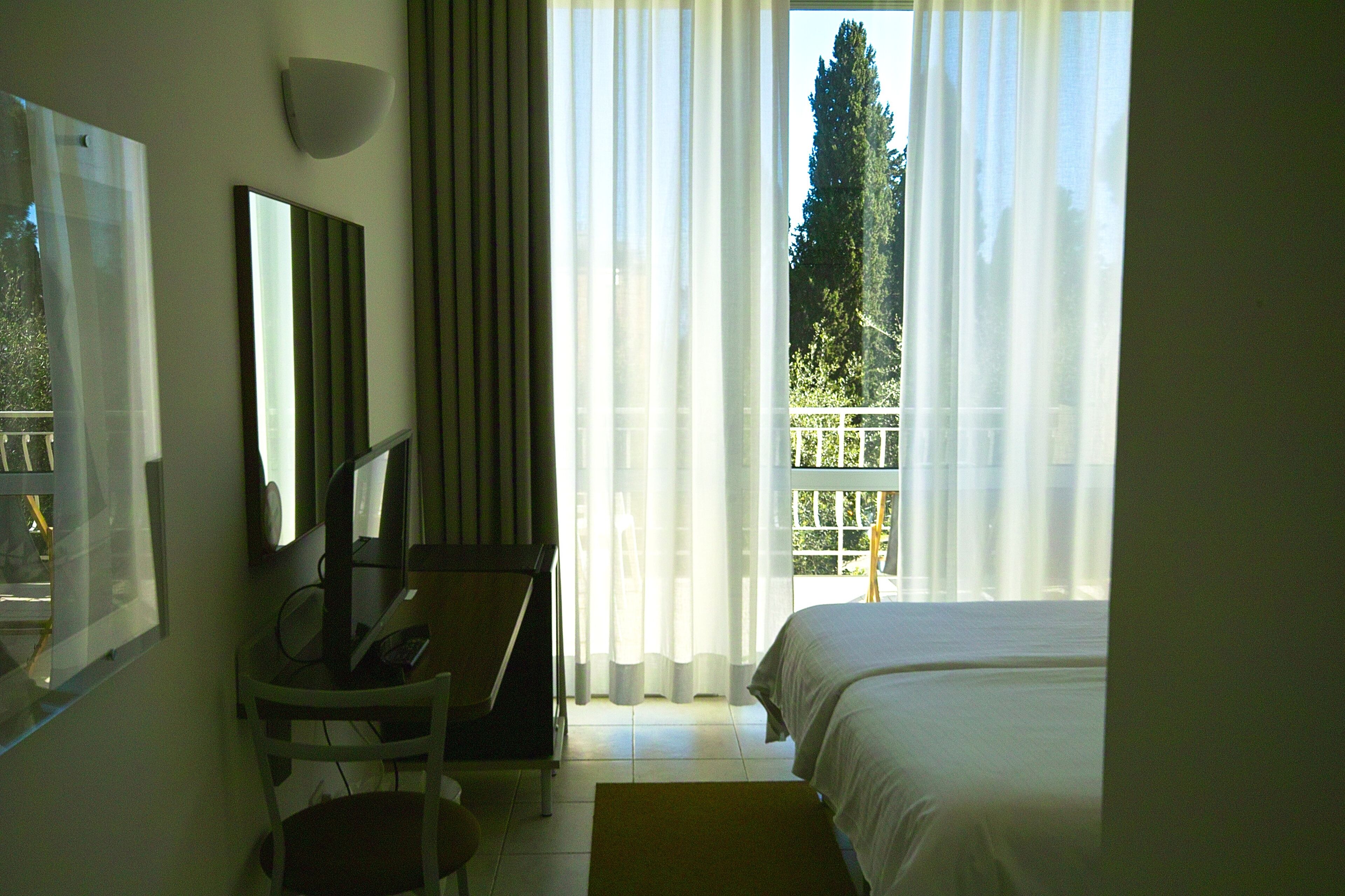 Une chambre d’hôtel avec un lit, un bureau avec un ordinateur, une chaise et une fenêtre avec des rideaux.