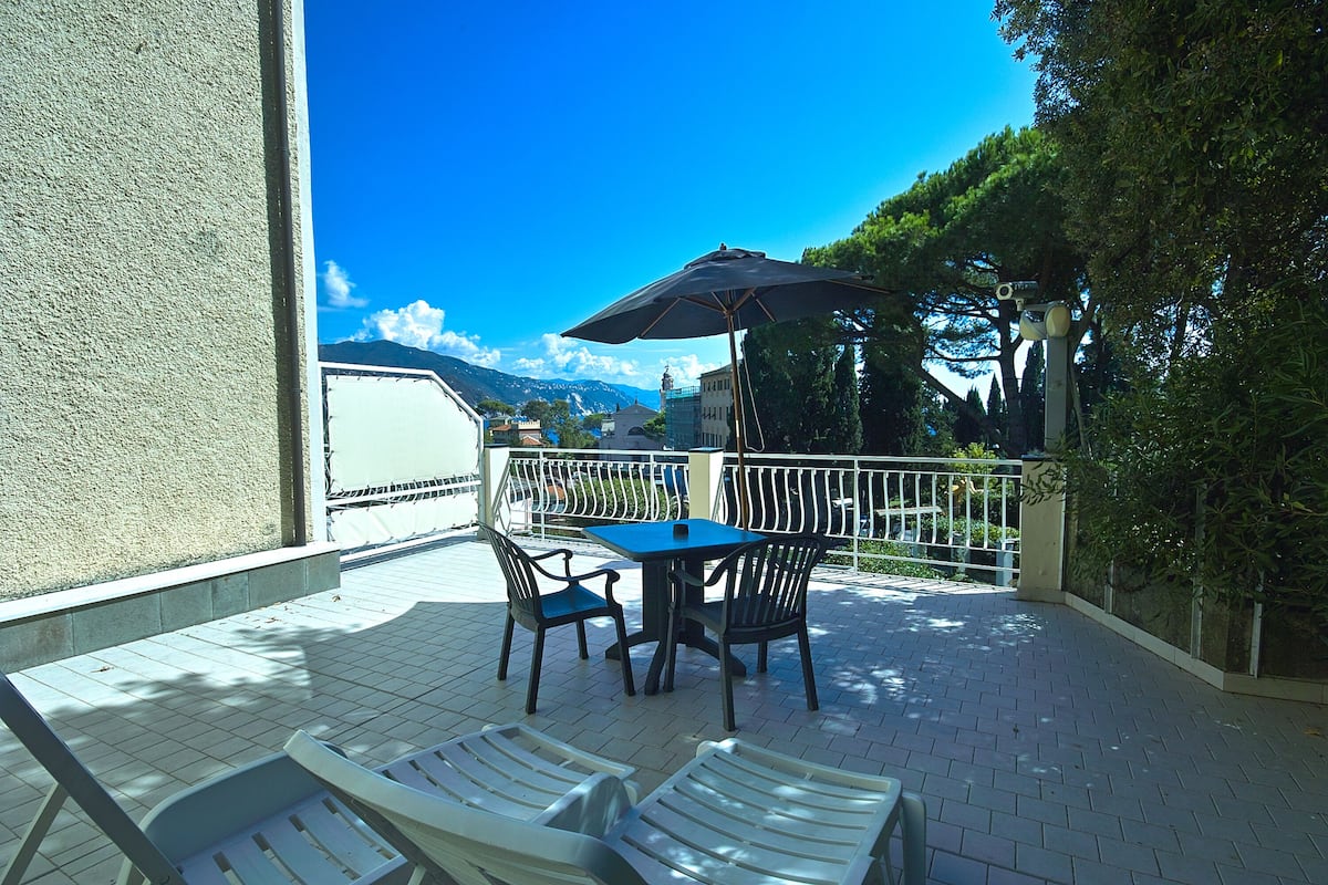 Eine Terrasse im Freien mit Tisch, Stühlen und einem großen Sonnenschirm, mit Blick auf Berge.