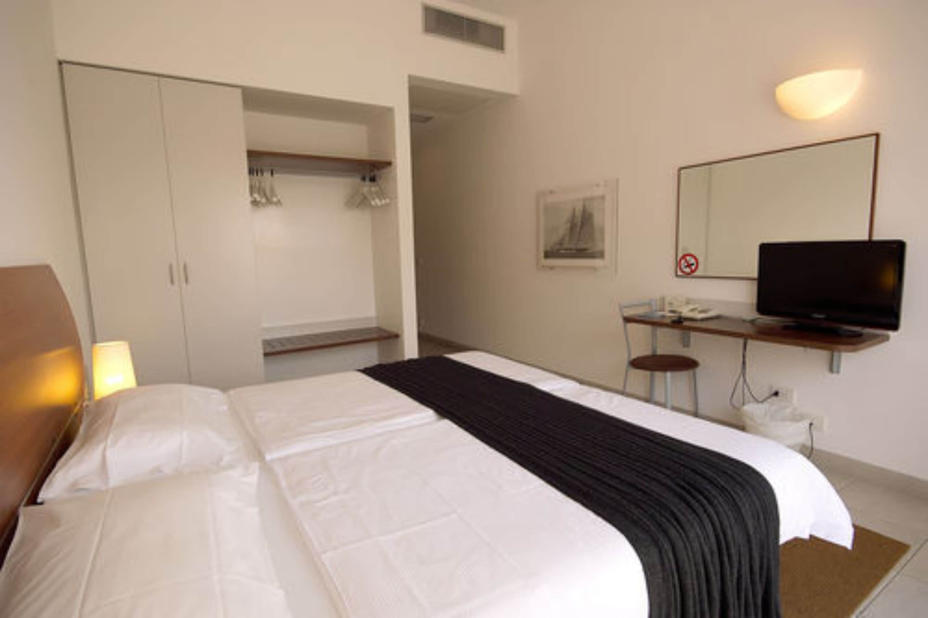 A hotel room with a bed, a desk with a computer, a television, and a wardrobe.