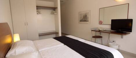 A hotel room with a bed, a desk with a computer, a television, and a wardrobe.