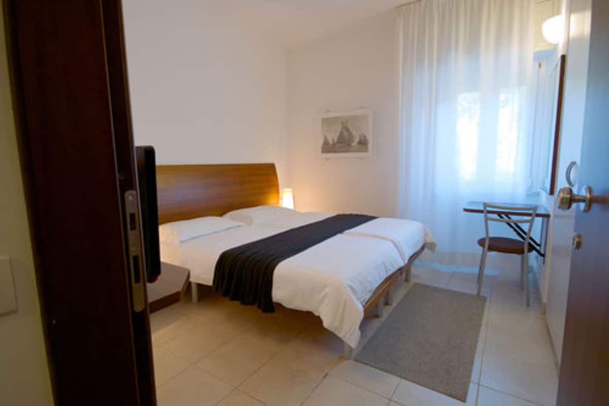 Ein Hotelzimmer mit Bett, Schreibtisch, Stuhl, Lampe und einem Bild an der Wand.