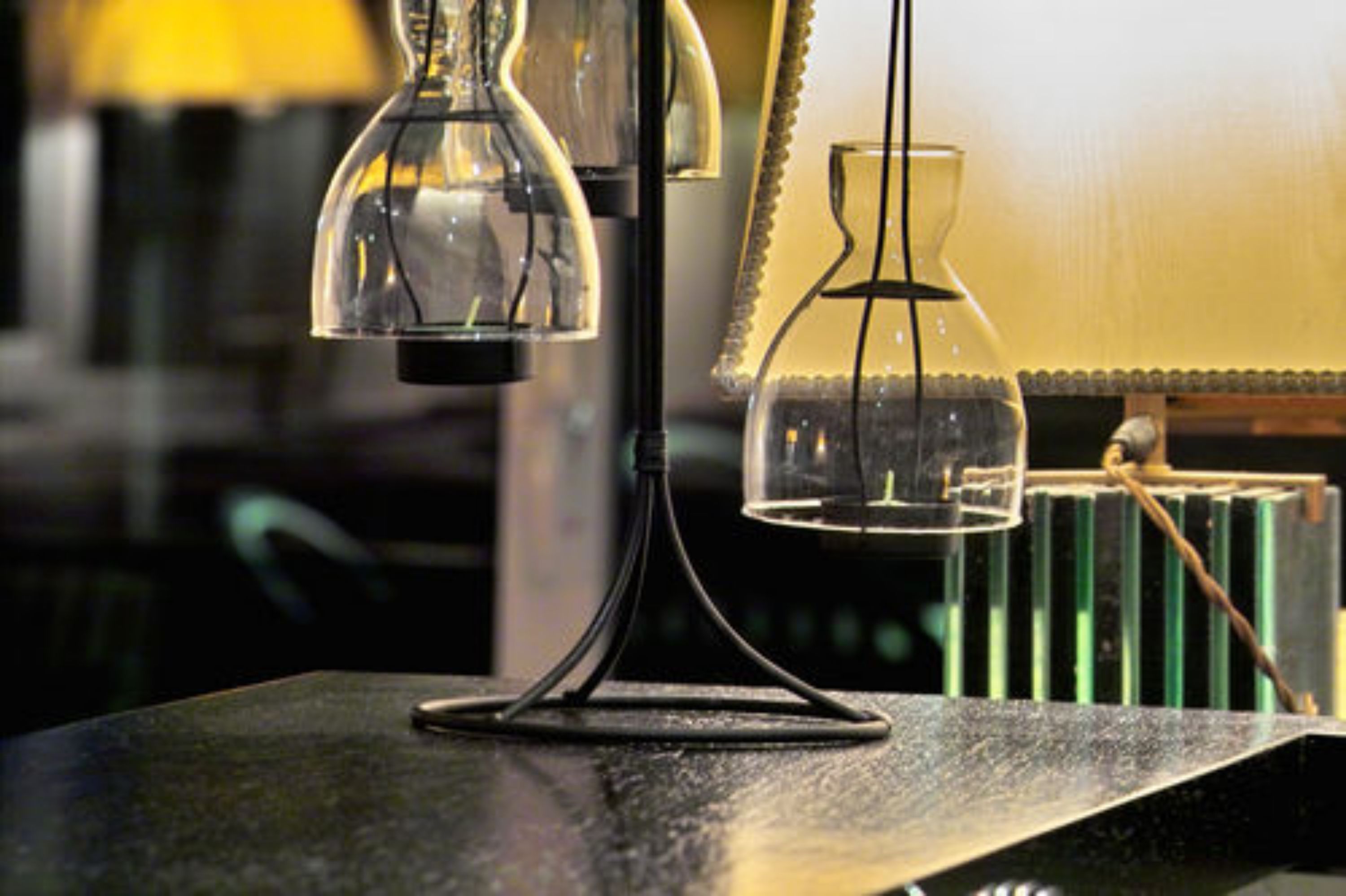 Une table surmontée de deux lampes en verre transparent, posée sur une surface sombre, peut-être dans une bibliothèque ou un espace de travail.