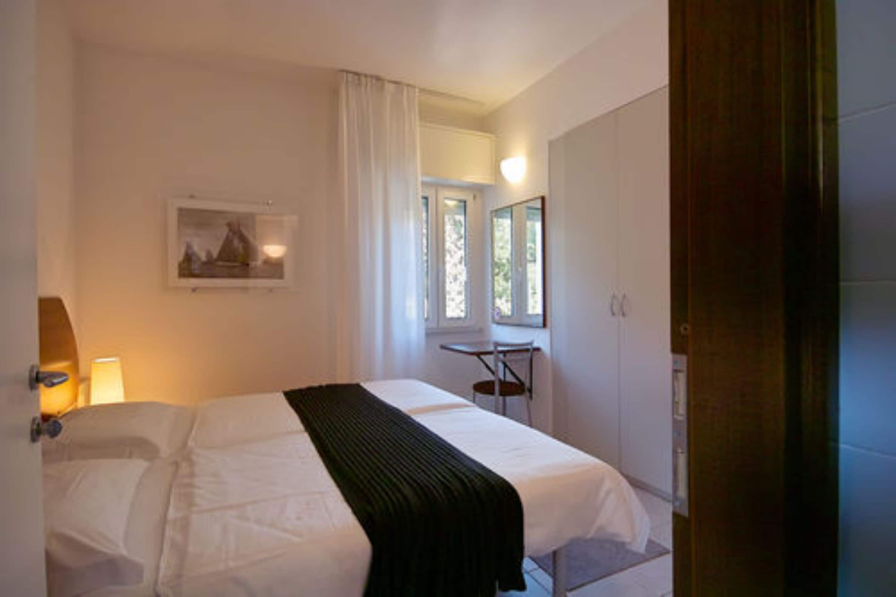 A hotel room with a bed, a desk, a chair, a window, and a picture on the wall.