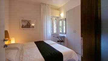 Una camera d'albergo con un letto, una scrivania, una sedia, una finestra e un quadro appeso al muro.