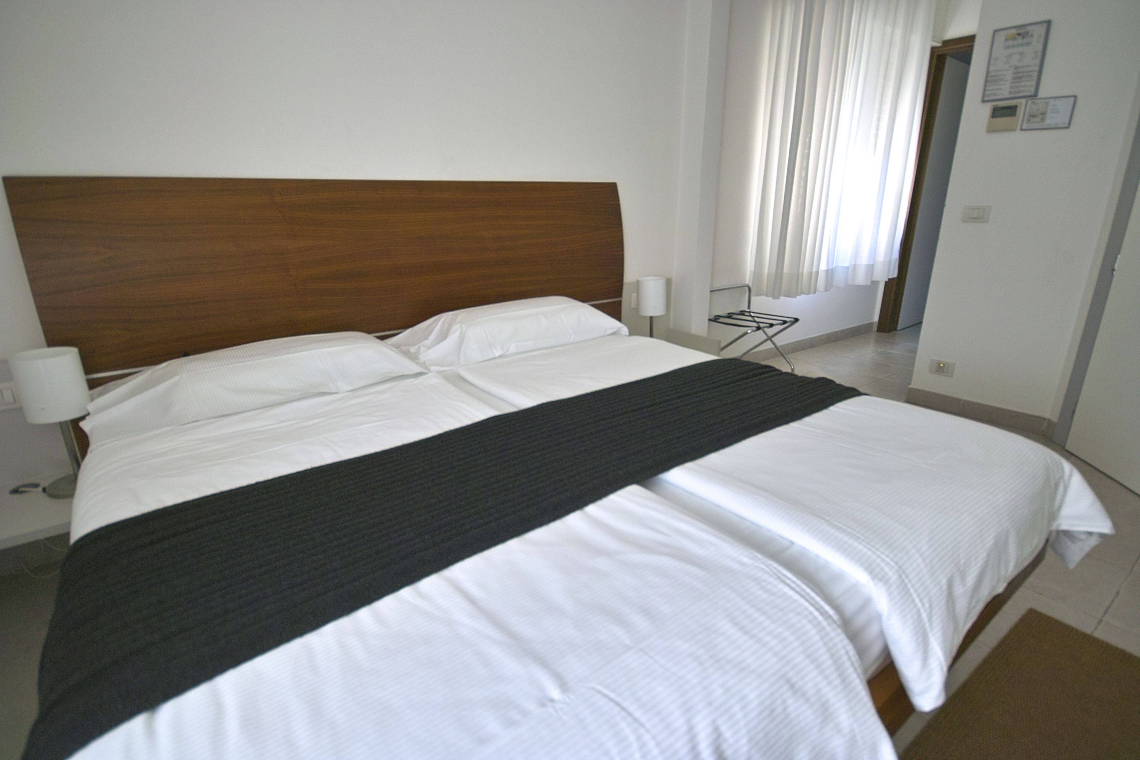 Een hotelkamer met een groot bed, een houten hoofdbord, witte lakens en een raam met gordijnen.