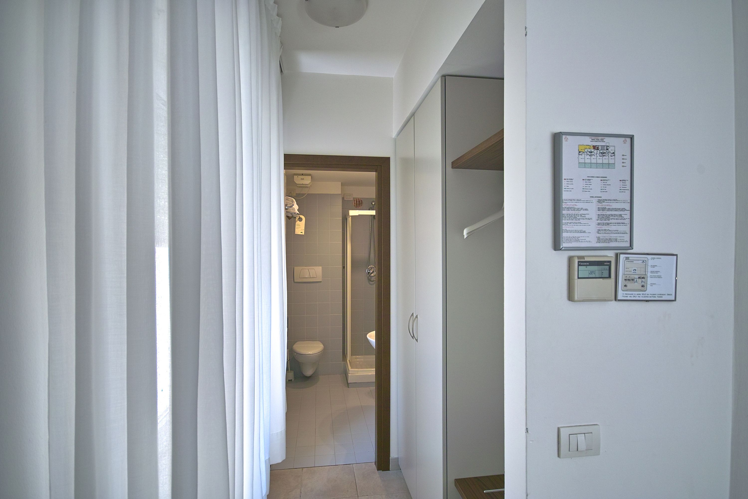 Ein Badezimmer mit Toilette, Dusche und einem an der Wand montierten Thermostat.
