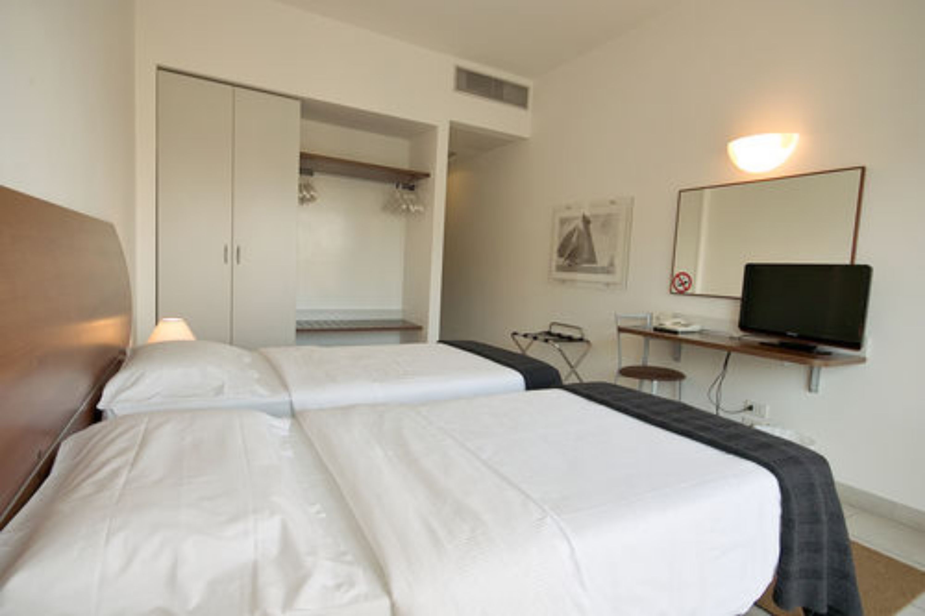 A hotel room with two beds, a desk with a computer, a television, and a wardrobe.