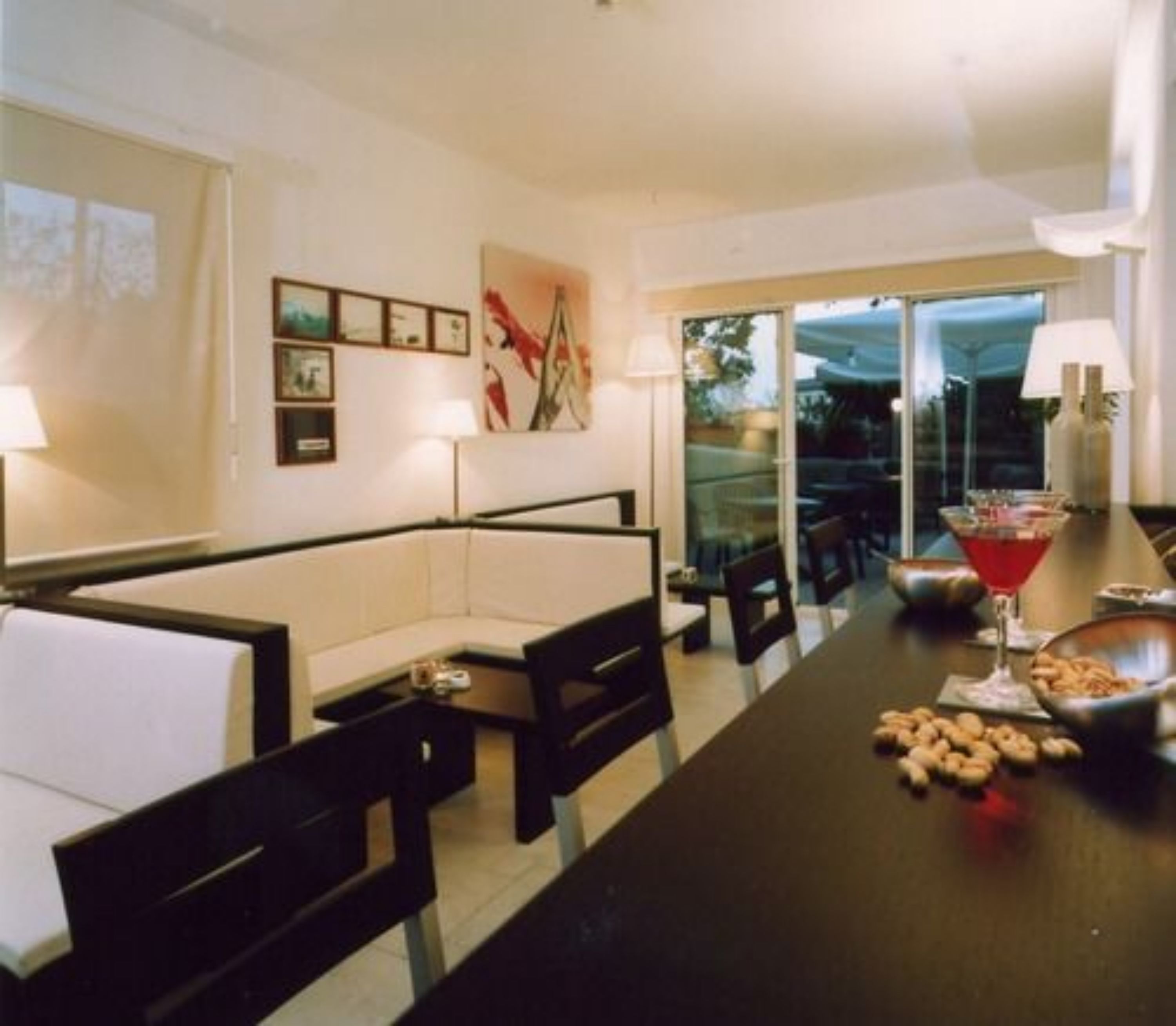 Un salon moderne avec un canapé, une table à manger et des chaises. Des tableaux encadrés ornent le mur, et une porte vitrée donne accès à un espace extérieur.