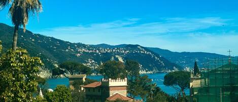 A coastal town with a prominent castle-like building, lush greenery, and a clear view of the sea.