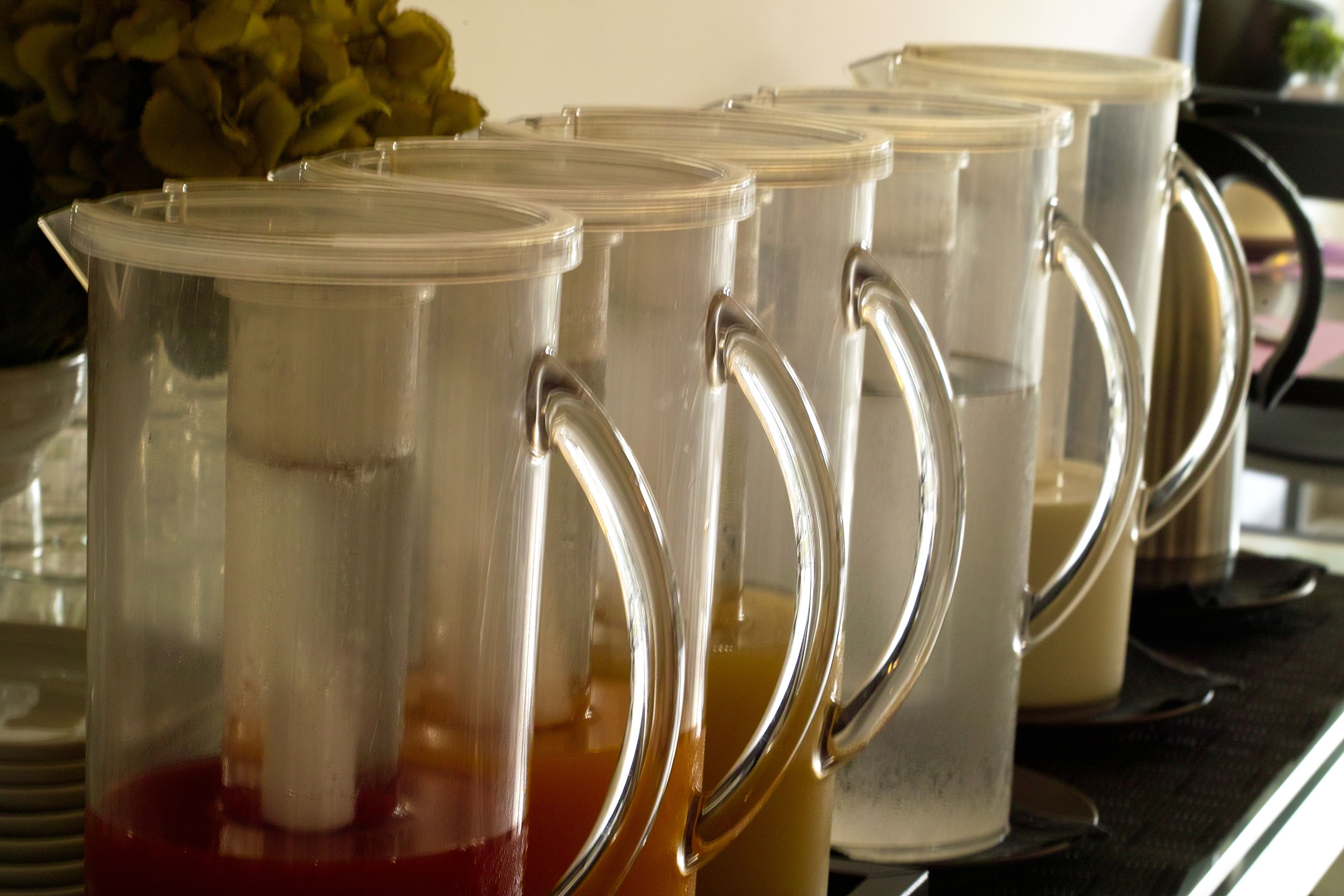 A row of clear glass dispensers with handles, likely for beverages, on a countertop.