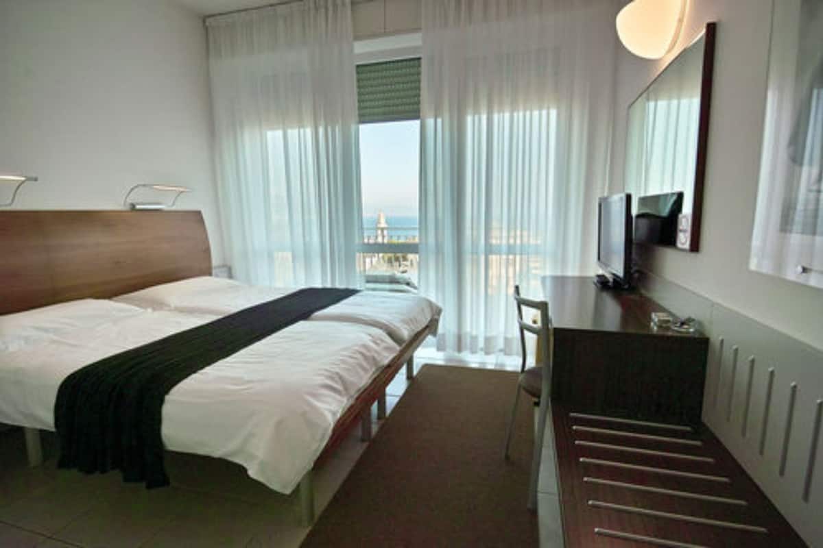 Ein Hotelzimmer mit Bett, Schreibtisch, Stuhl, Fernseher und Blick auf die Stadt durch das Fenster.