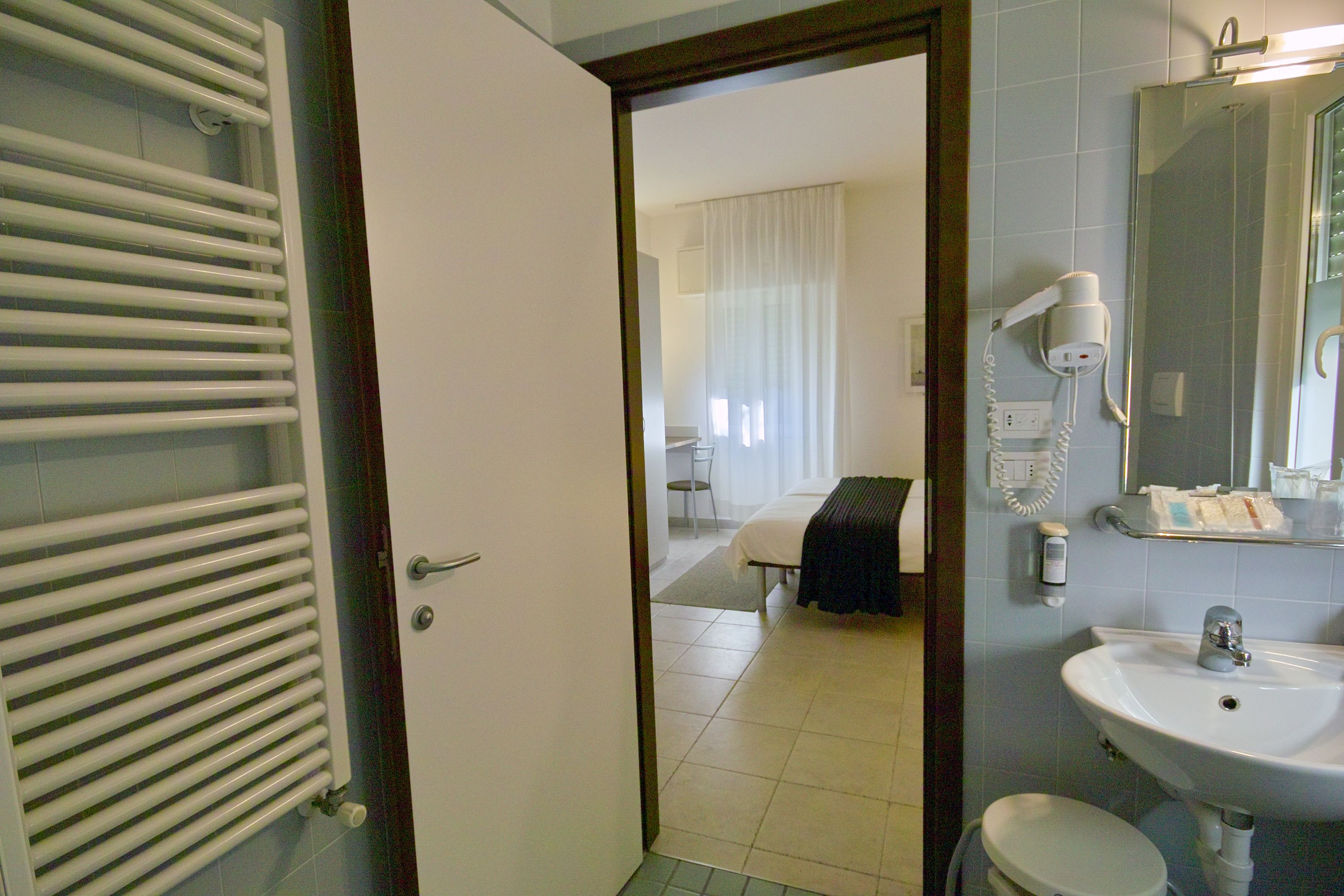 Une salle de bain d’hôtel avec un lavabo blanc, un miroir et un sèche-cheveux fixé au mur.