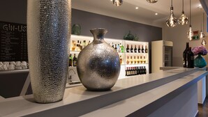 A bar area with a large metallic vase, a wine bottle display, and hanging light fixtures. - Hotel Capolago (Varese)