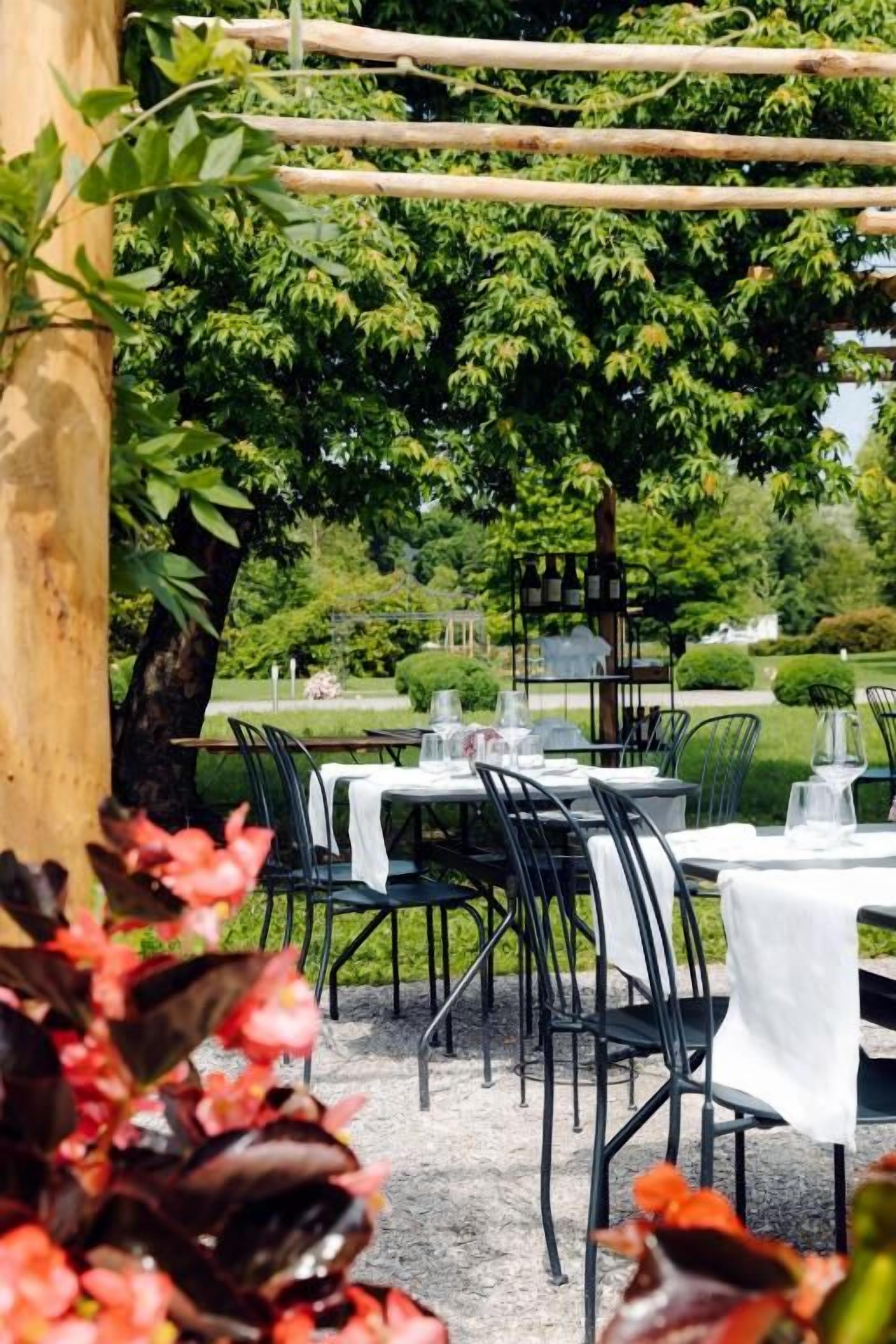 Un área de comedor al aire libre con mesas y sillas, rodeada de follaje y árboles.