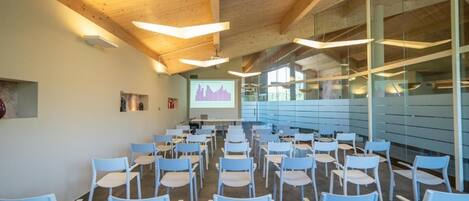 A conference room with rows of chairs, a projector screen, and a presentation.