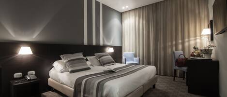 A modern hotel room with a large bed, bedside lamps, a desk with a telephone, and a chair.
