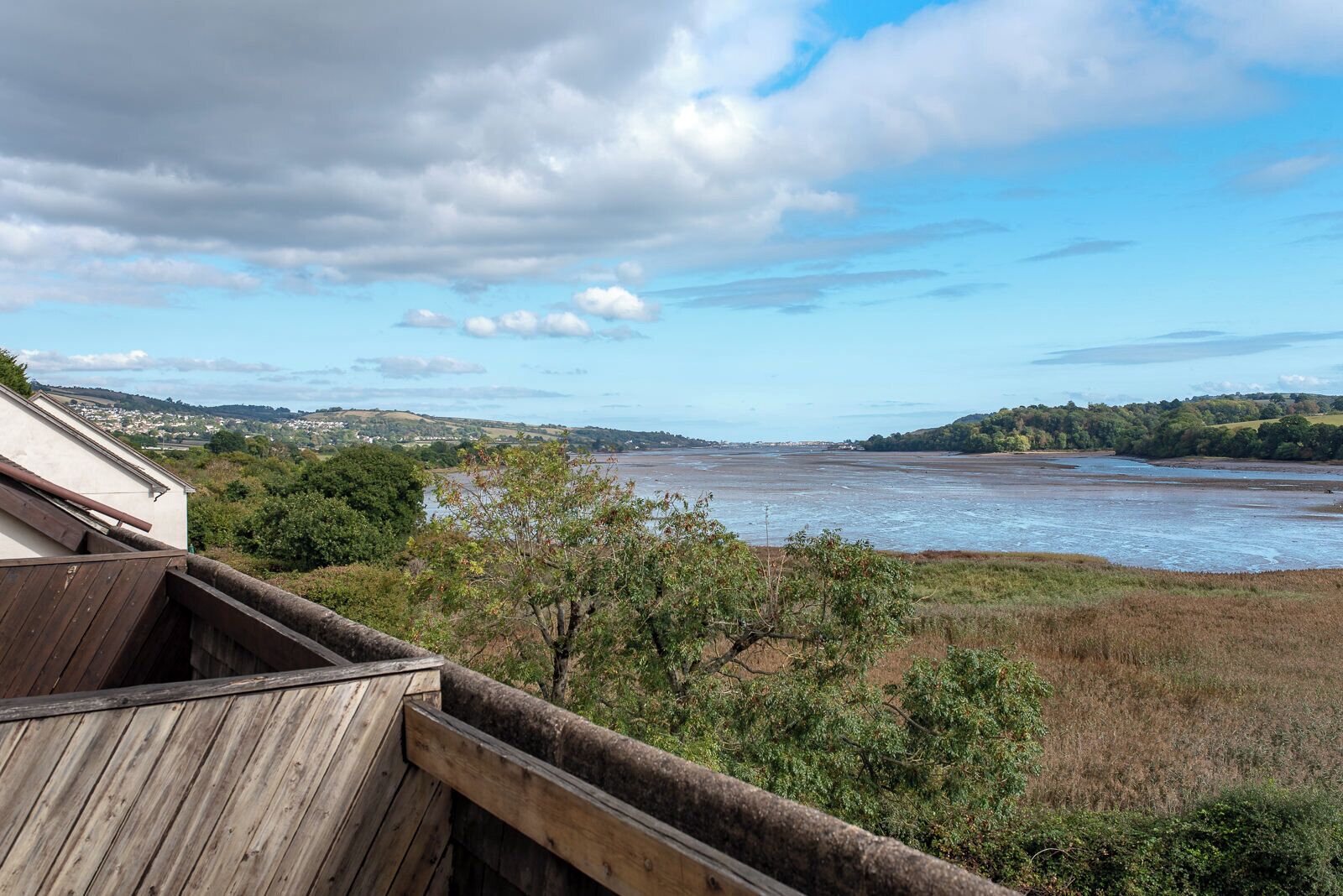 Ein Küstenblick mit einer Holzterrasse mit Blick auf einen Strand und eine in der Ferne liegende Stadt.