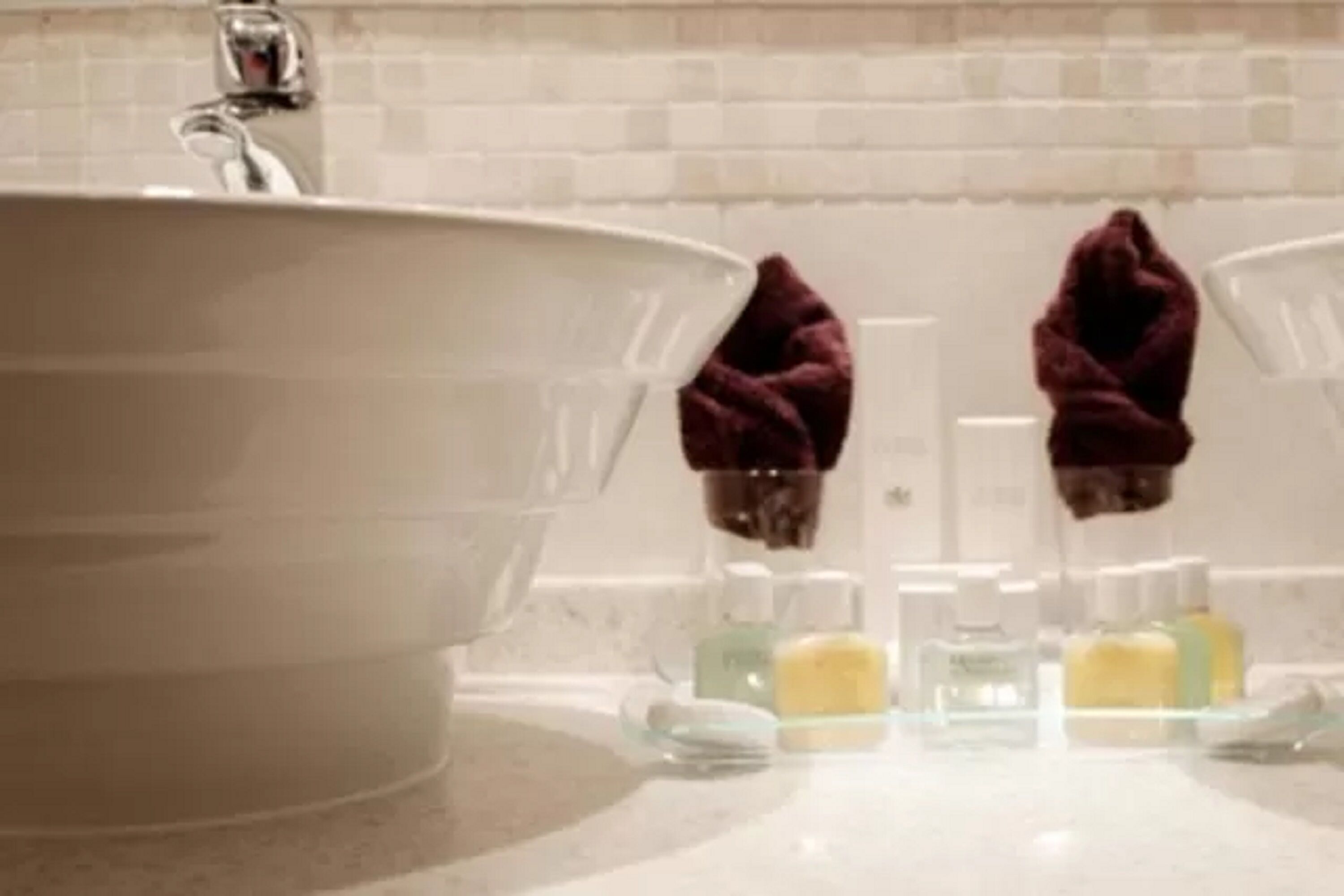 A bathroom with a large sink, two mirrors, and toiletries on the counter.
