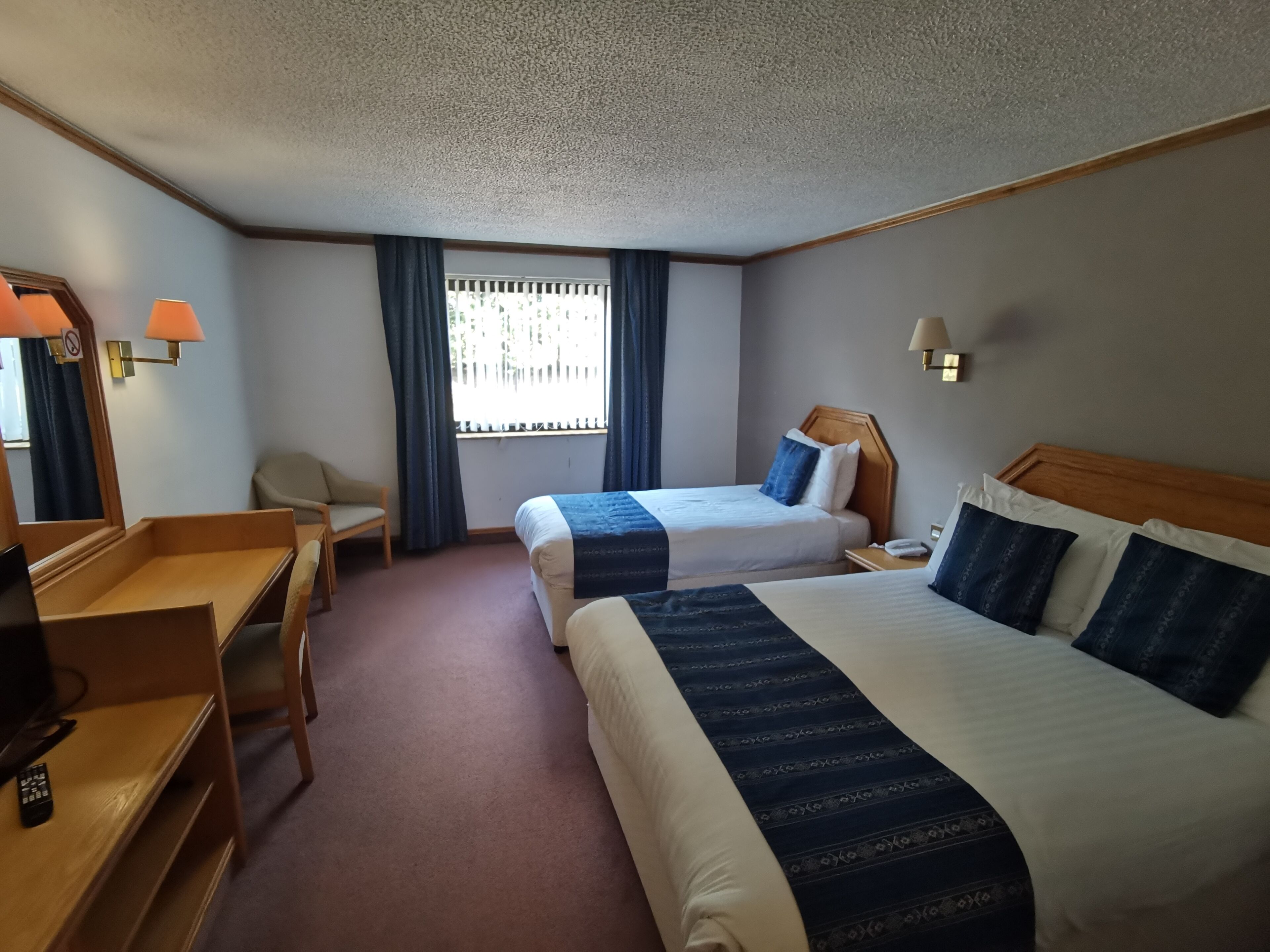 A hotel room with two beds, a desk, a chair, a TV, and a window with curtains.