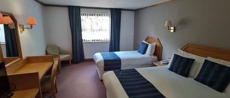 A hotel room with two beds, a desk, a chair, a TV, and a window with curtains.