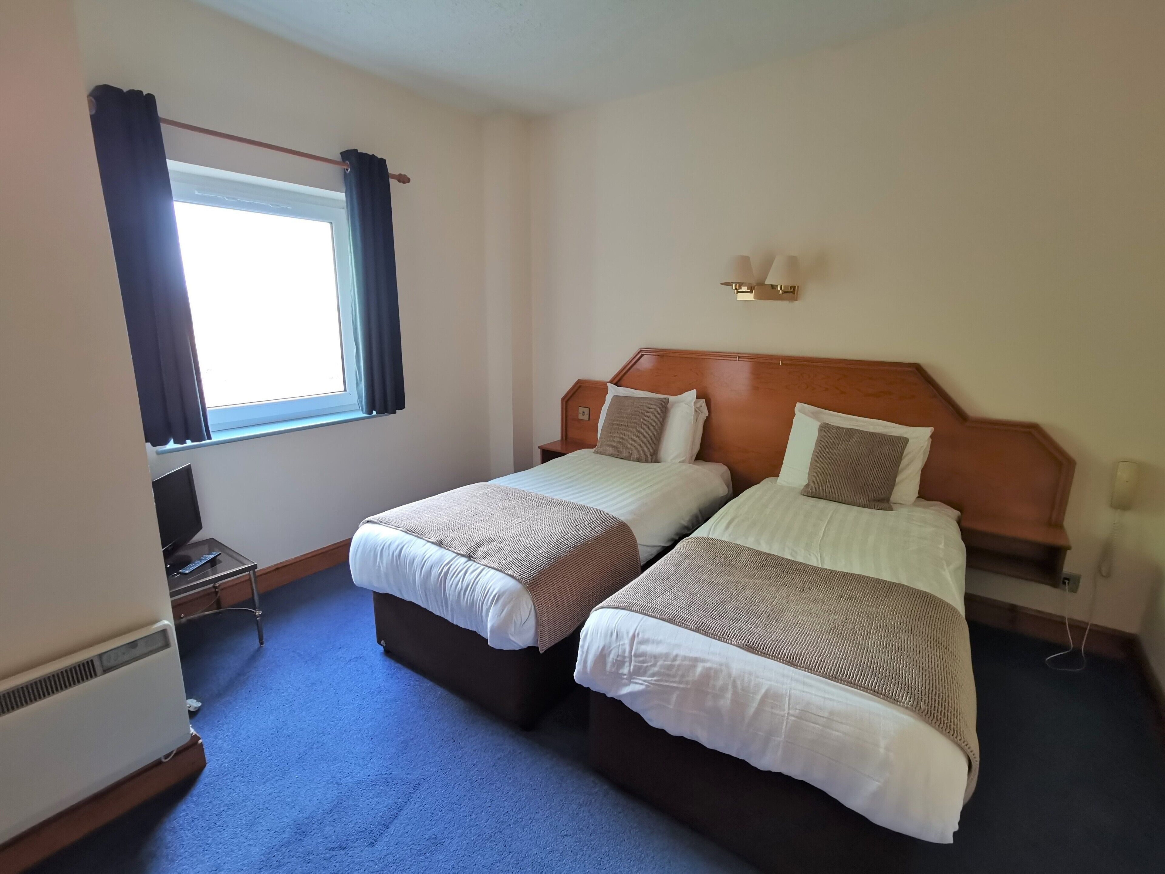 Habitación de hotel con dos camas, televisión, calefacción y ventana con cortinas.