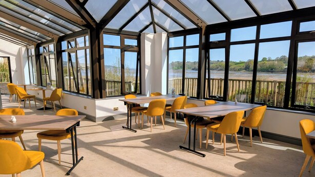 A spacious indoor area with large windows, tables, and chairs arranged for dining or meetings.