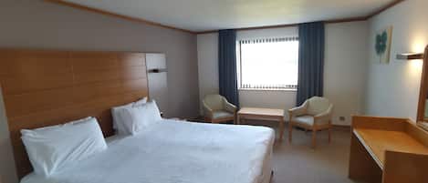 Habitación de hotel con una cama grande, dos sillas, una mesita, un escritorio y una ventana con cortinas.