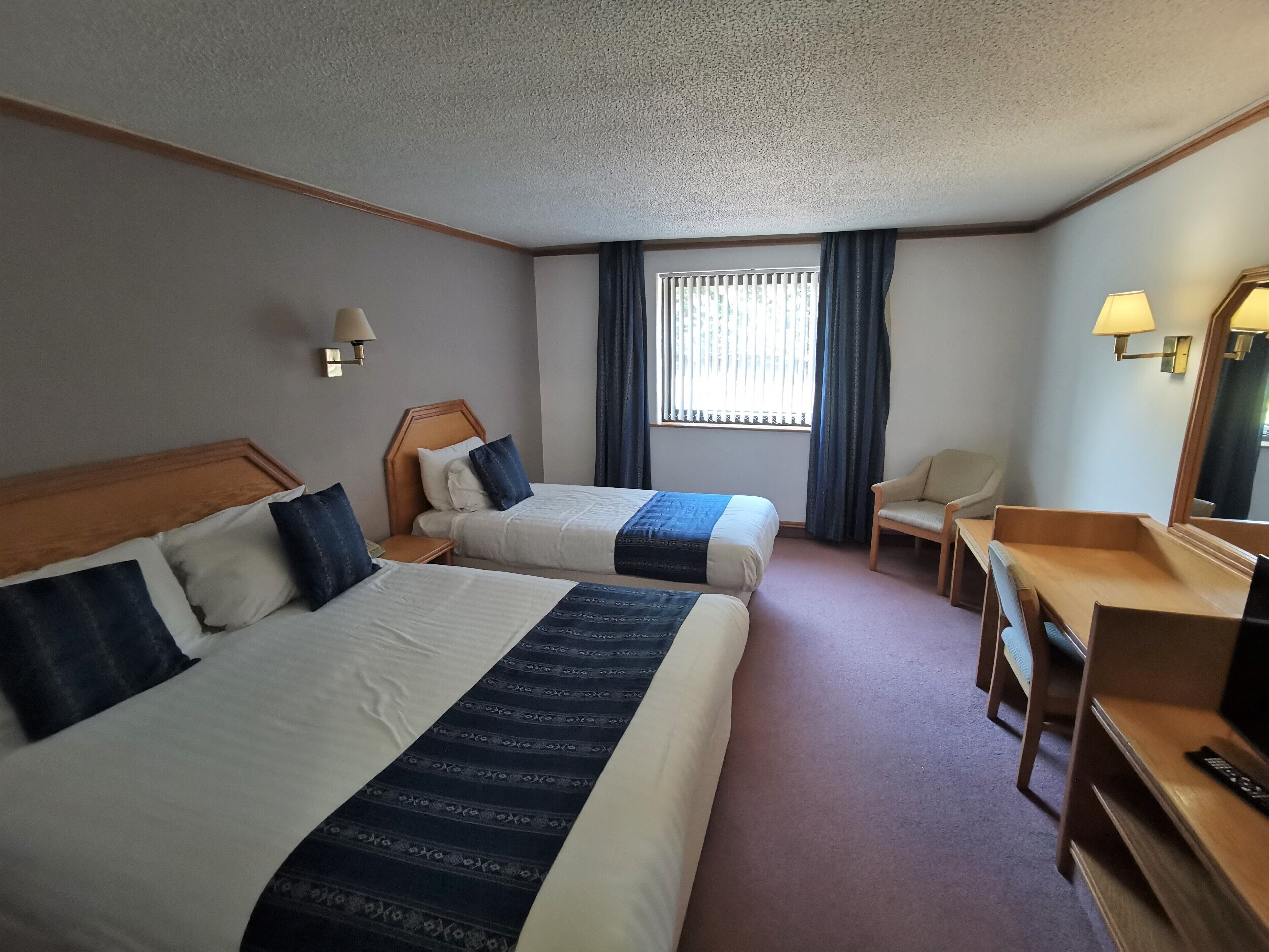 Une chambre d’hôtel avec deux lits, un bureau, une chaise, une télévision et une fenêtre avec des rideaux.