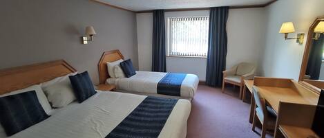 Een hotelkamer met twee bedden, een bureau, een stoel, een televisie en een raam met gordijnen.