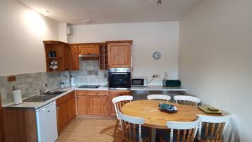 A kitchen with wooden cabinets, a built-in oven, a microwave, and a dining table with chairs.