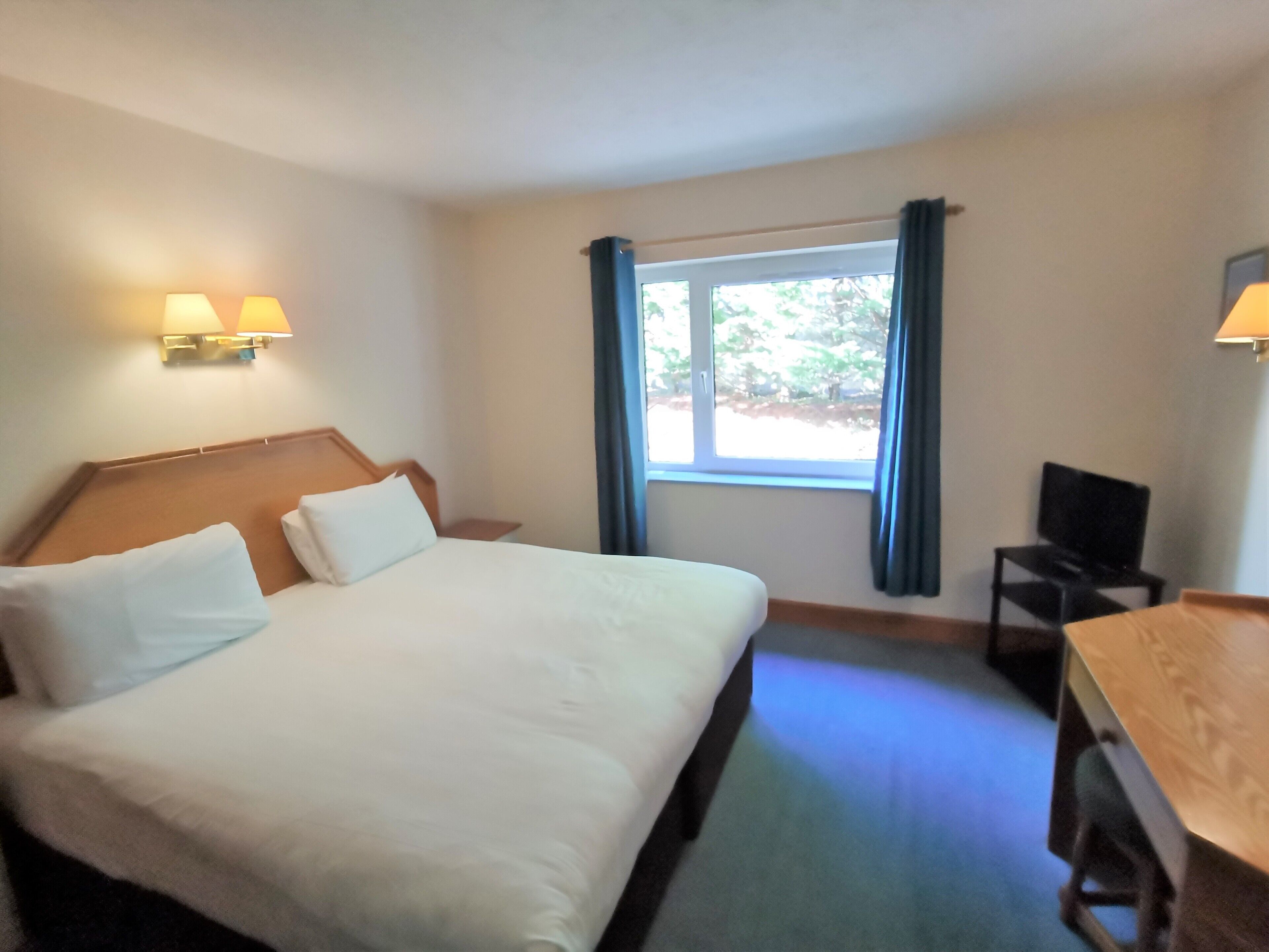 A hotel room with a large bed, a desk, a chair, and a window with curtains.