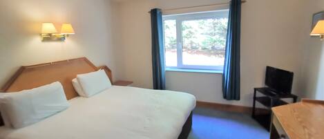 Una habitación de hotel con una cama grande, un escritorio, una silla y una ventana con cortinas.