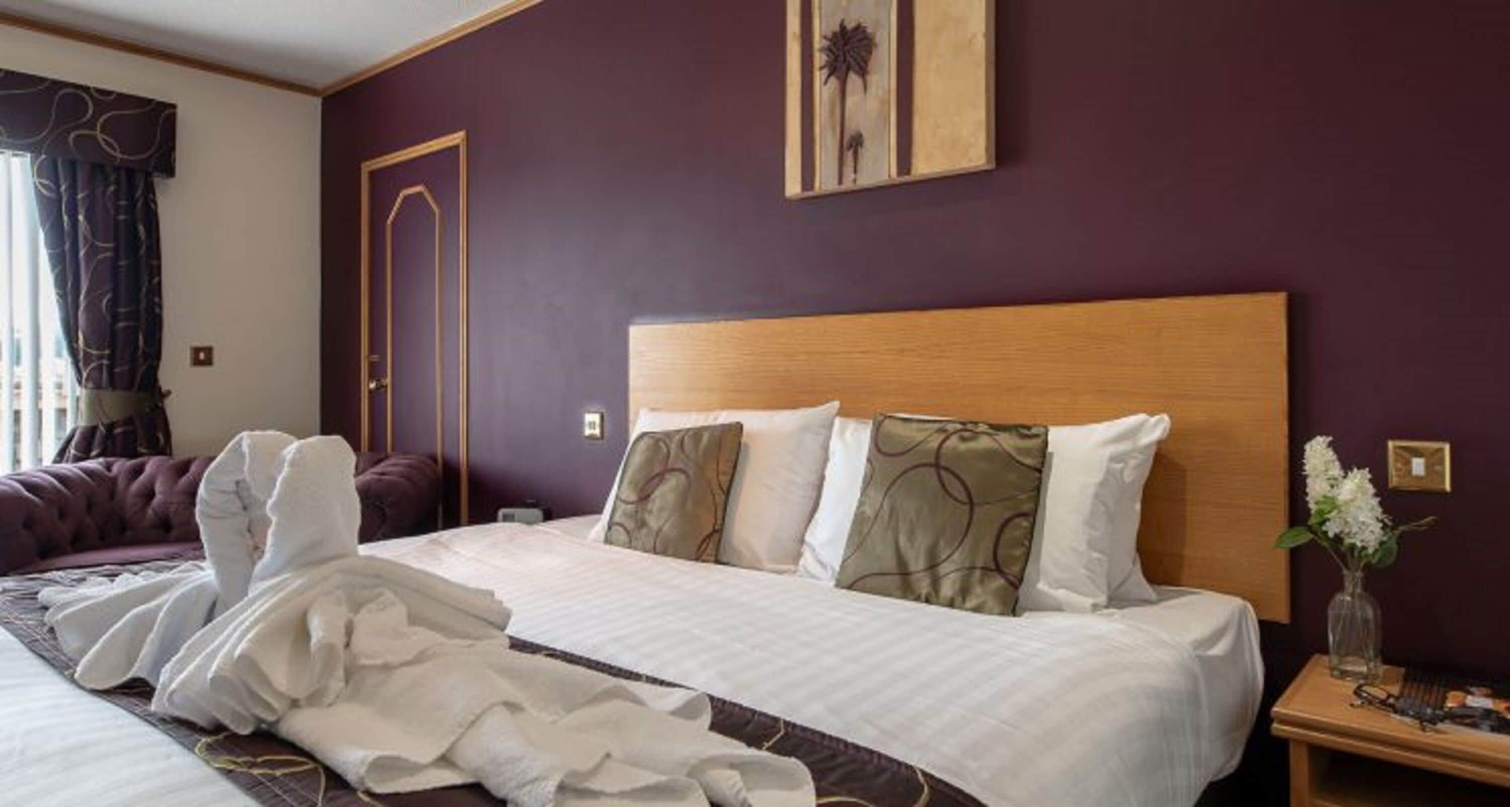 A hotel room with a large bed, a wooden headboard, and a nightstand with a vase of flowers.