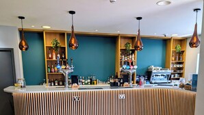 A bar area with a curved counter, multiple taps, shelves with bottles, and a coffee machine.