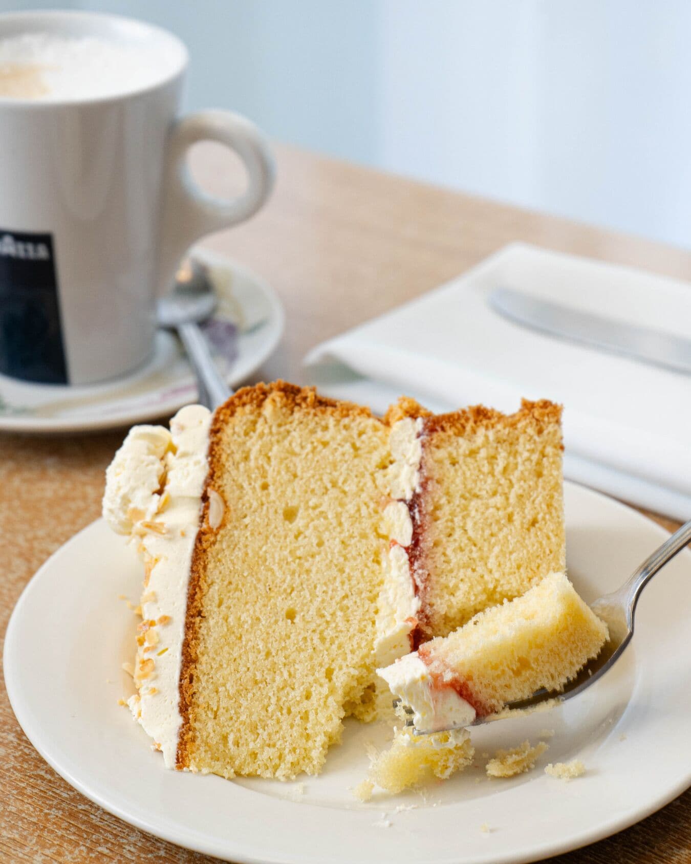 A slice of cake on a plate with a spoon, a cup of coffee, and a napkin on a table.