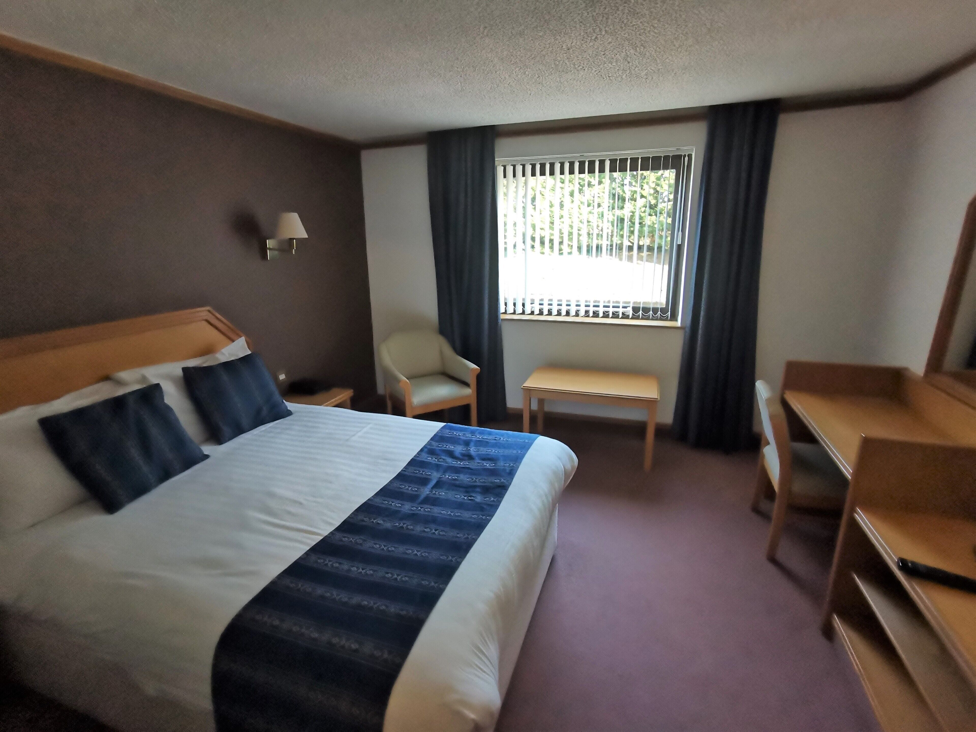 Une chambre d’hôtel avec un grand lit, un bureau, une chaise et une fenêtre avec des rideaux.