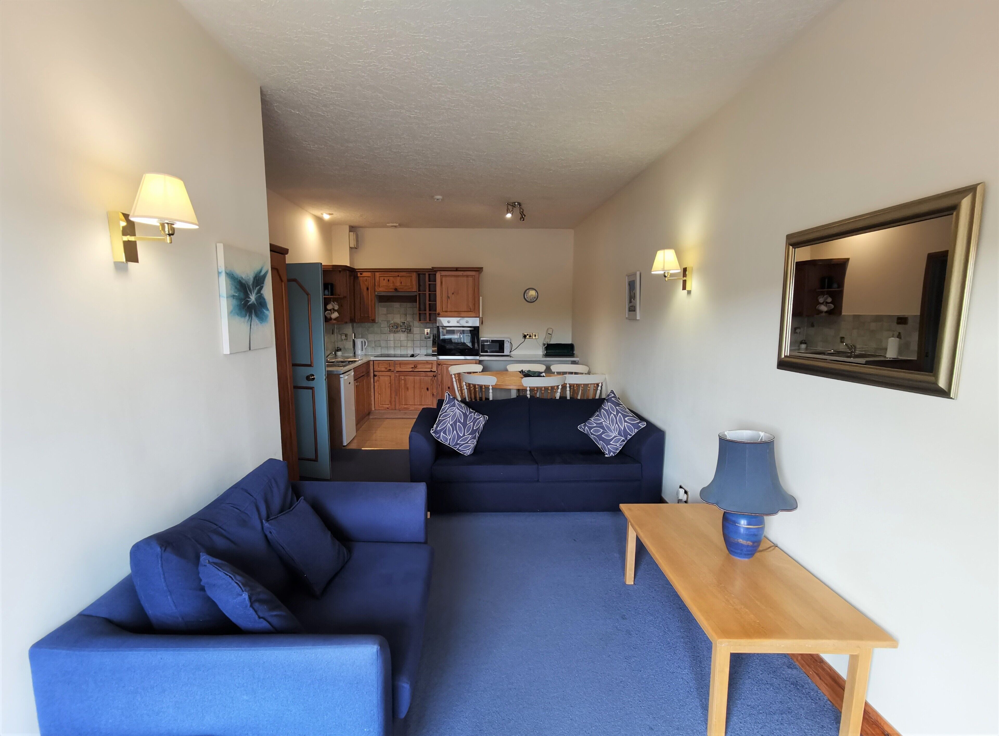 A compact living space with a sofa, a small table, and a kitchenette in the background.