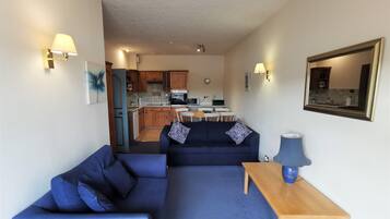 A compact living space with a sofa, a small table, and a kitchenette in the background.