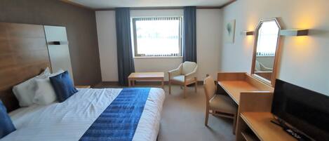 A hotel room with a bed, a desk, a chair, a TV, and a window with curtains.