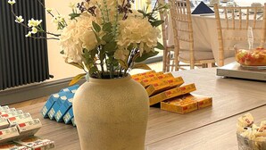 A dining area with a large window, a vase of flowers, and various food items on the table.