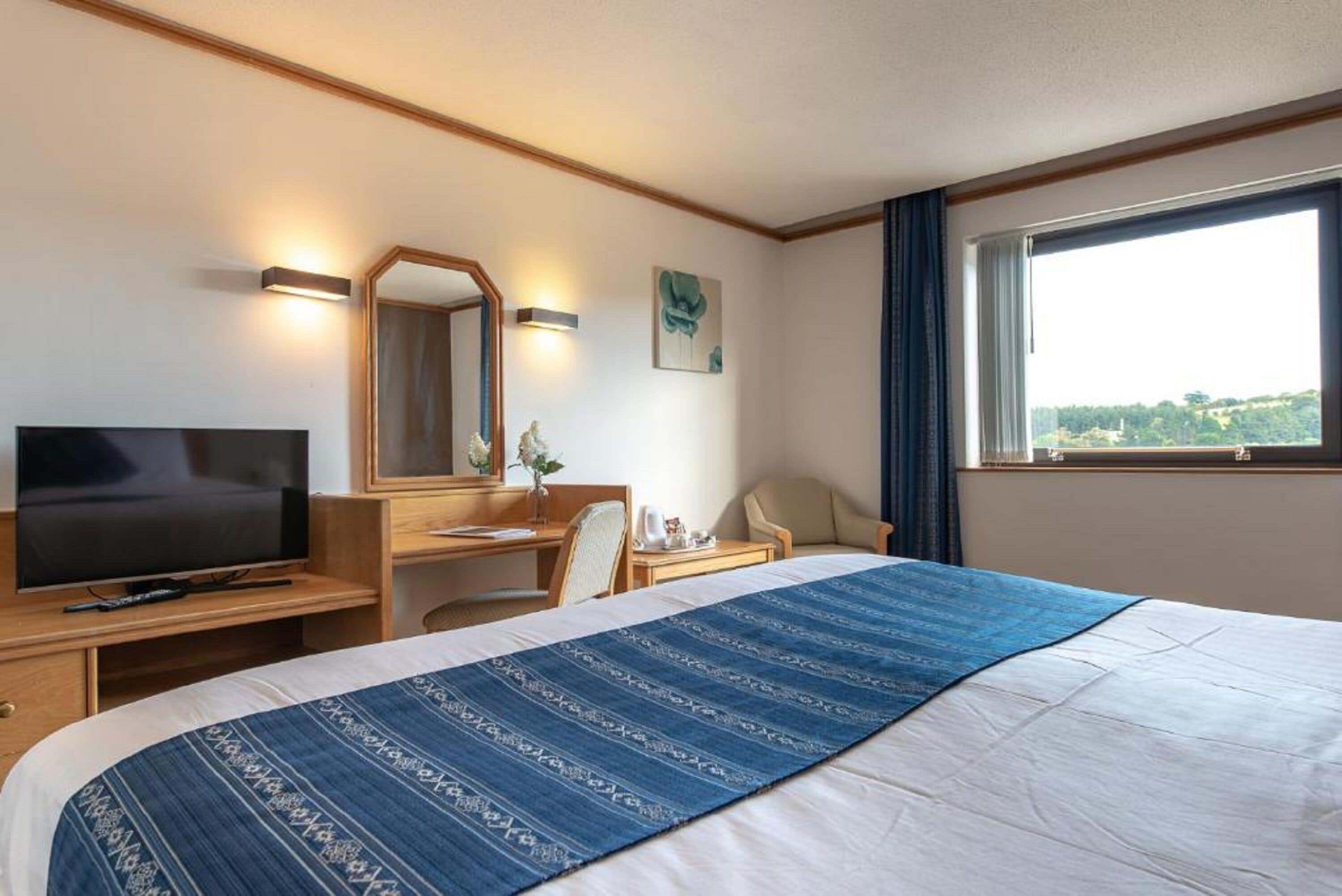 Ett hotellrum med en säng, ett skrivbord, en stol, en tv och ett fönster med utsikt.