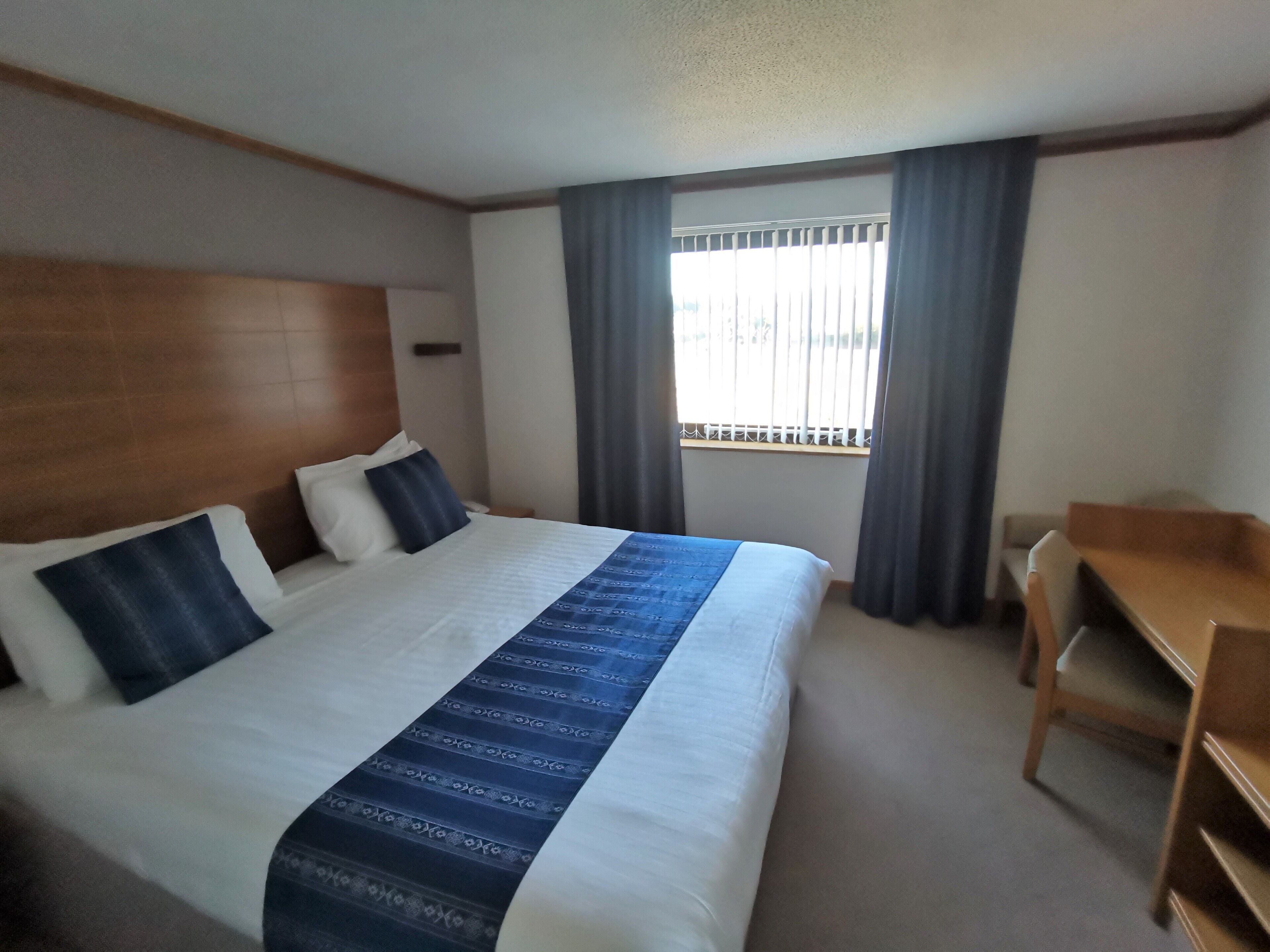 A hotel room with a large bed, a desk, and a window with curtains.
