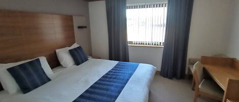 A hotel room with a large bed, a desk, and a window with curtains.
