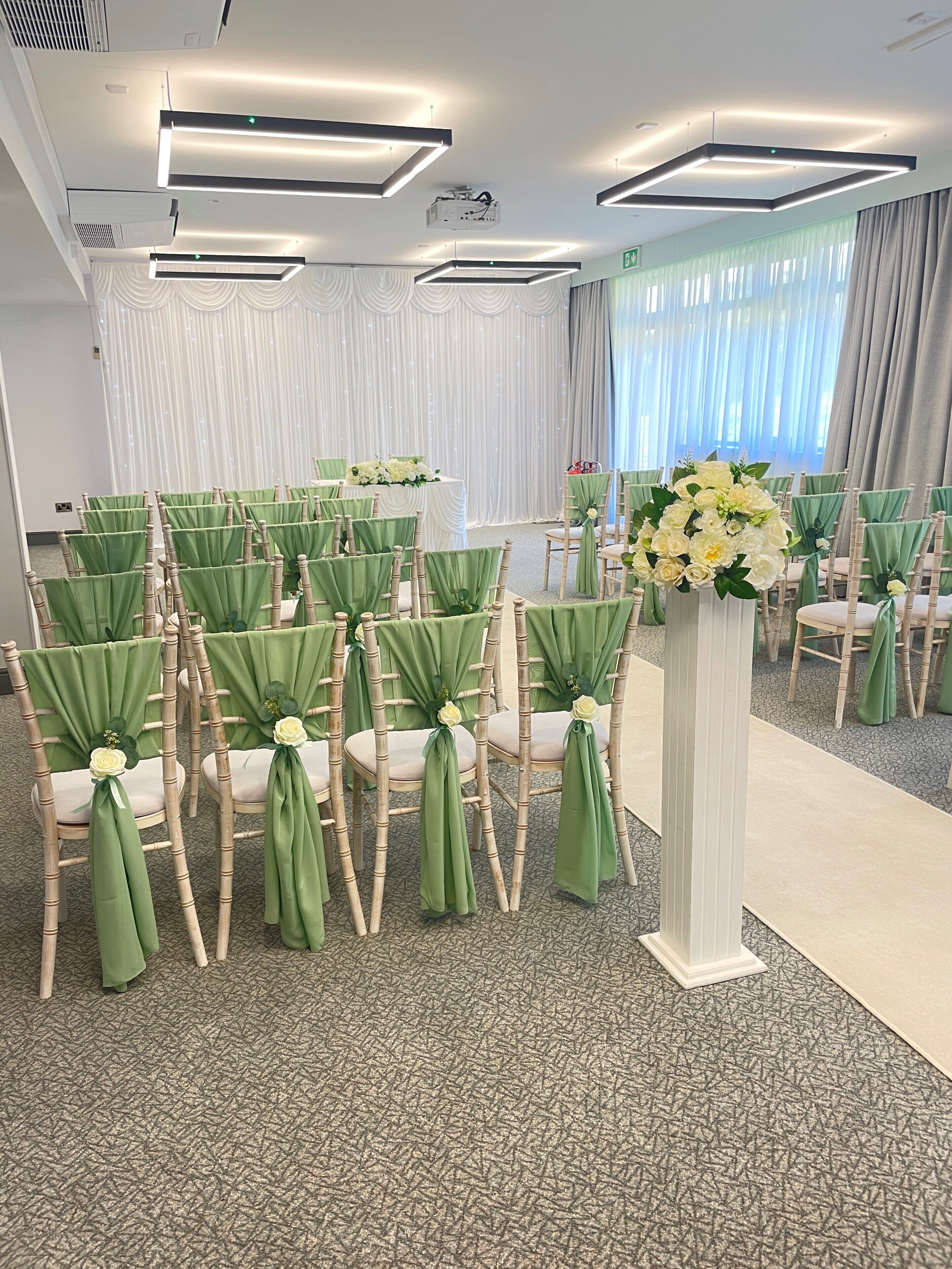 A conference room with rows of chairs, a white podium, and a large window with curtains.