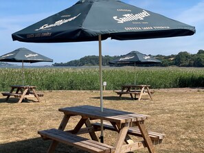 Outdoor picnic tables with attached umbrellas, set in a grassy area with a view of a water body and distant hills. - Passage House Hotel (Newton Abbot)