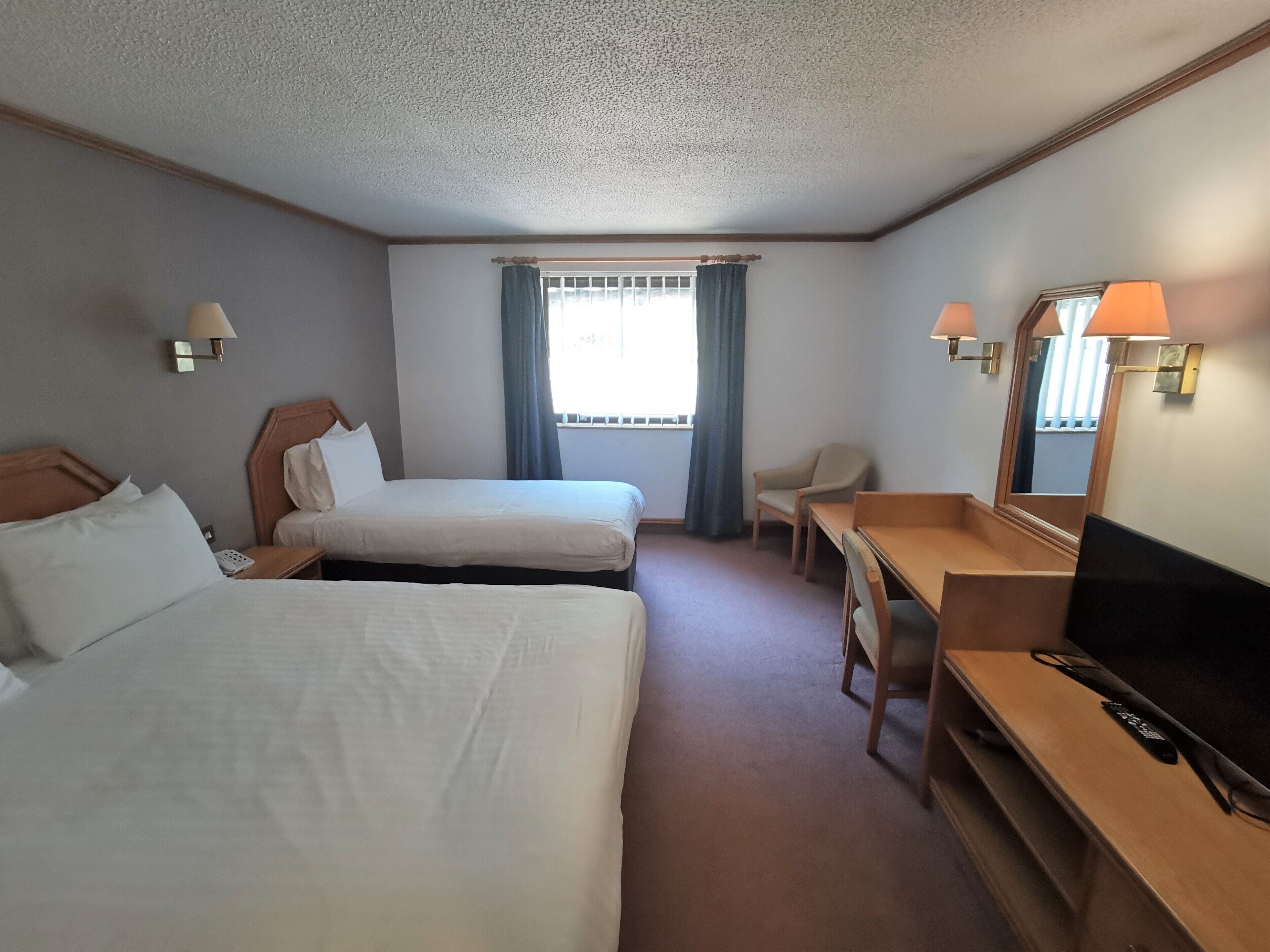 Une chambre d’hôtel avec deux lits, un bureau, une chaise, une télévision et une fenêtre avec des rideaux.