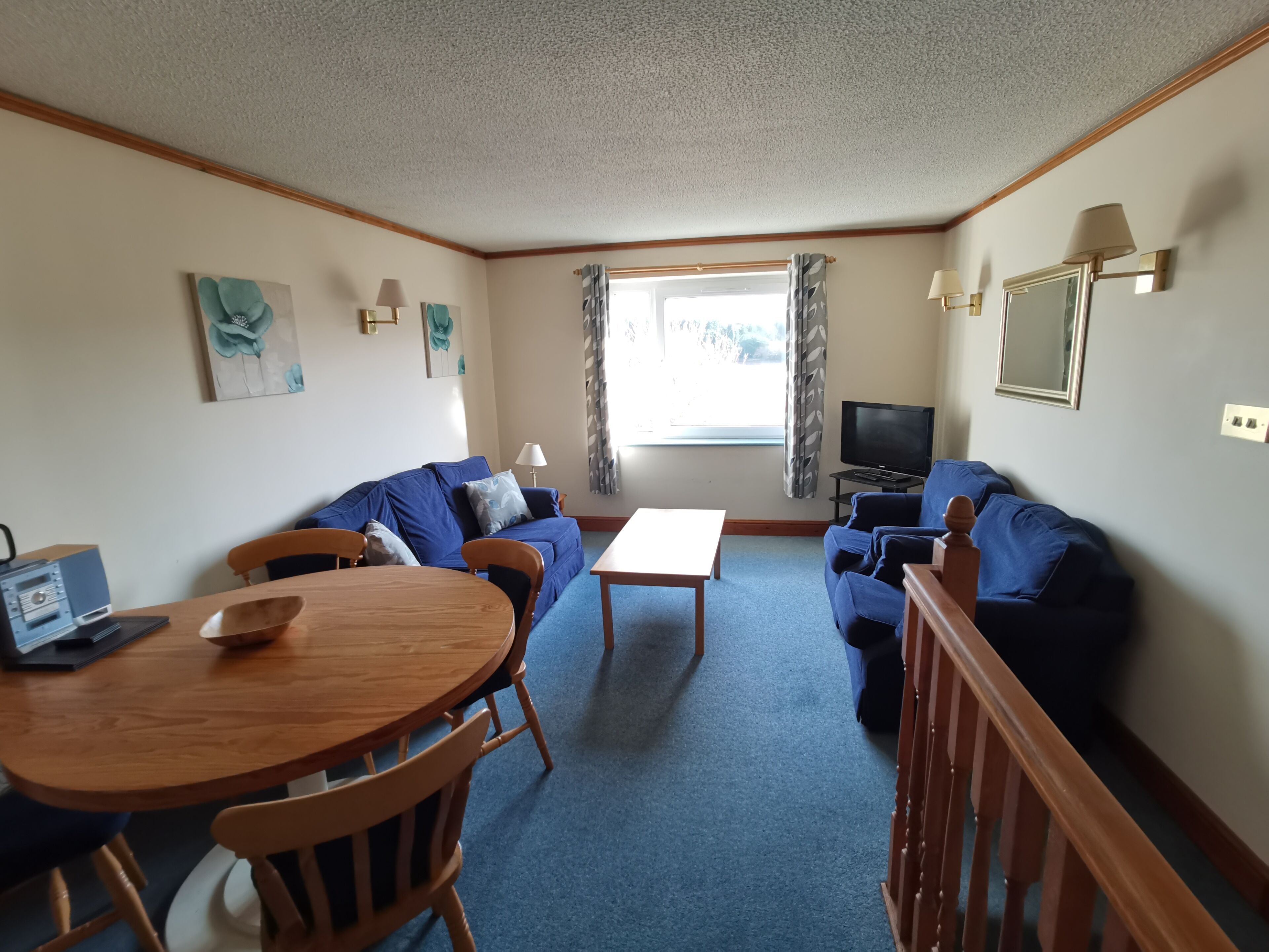 A compact living room with a blue sofa, a wooden dining table, and a television.