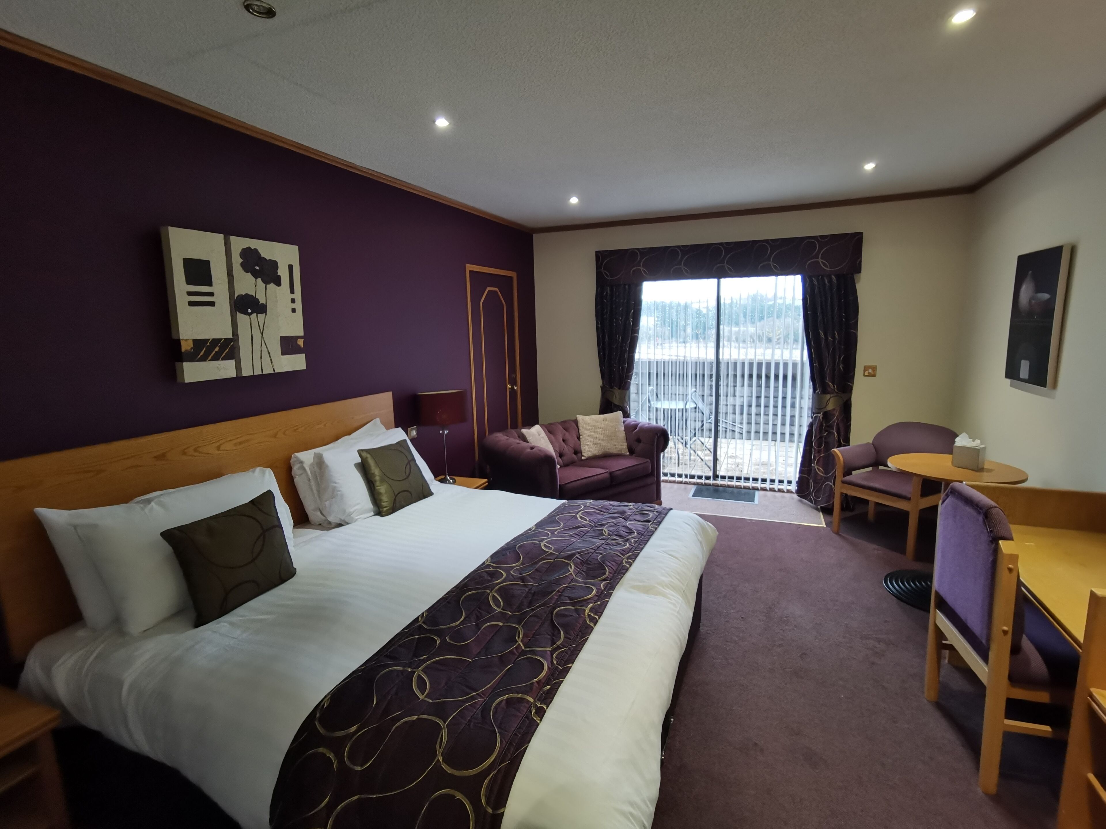 A hotel room with a large bed, a sofa, a small table, and a balcony with a view.