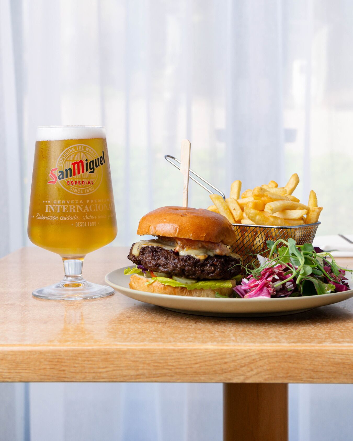 A meal with a burger, fries, and a beer glass on a wooden table.