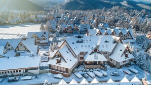 A snow-covered village with traditional chalet-style buildings, a parking area, and mountains in the background. - Skalny (Zakopane)